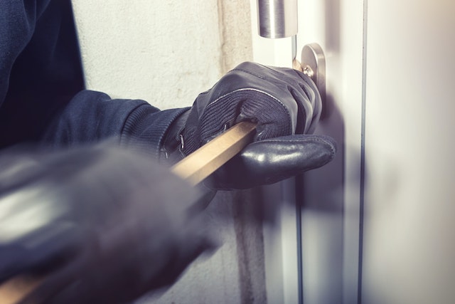 person with gloves using a crowbar to break into a home